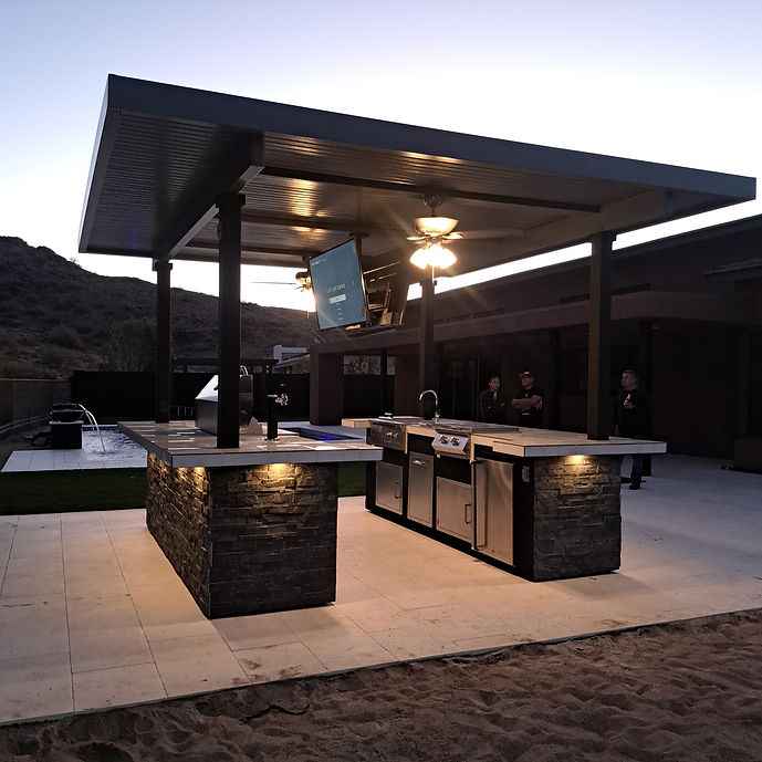 Outdoor kitchen island at dusk with a mounted TV and built-in grill.