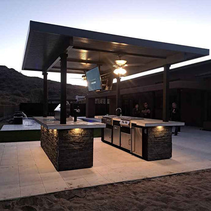 Outdoor kitchen island at dusk with a mounted TV and built-in grill.