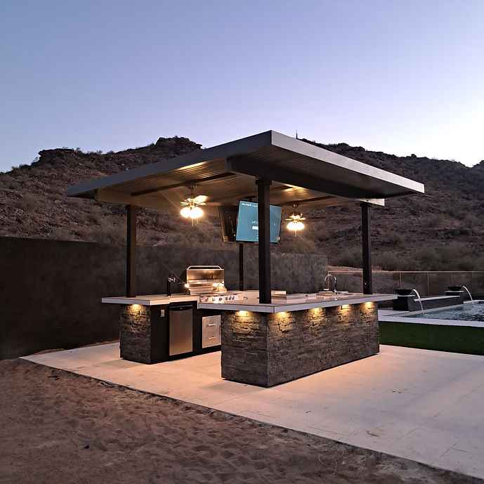 Angled view of the outdoor kitchen island with built-in grill and mounted TV.