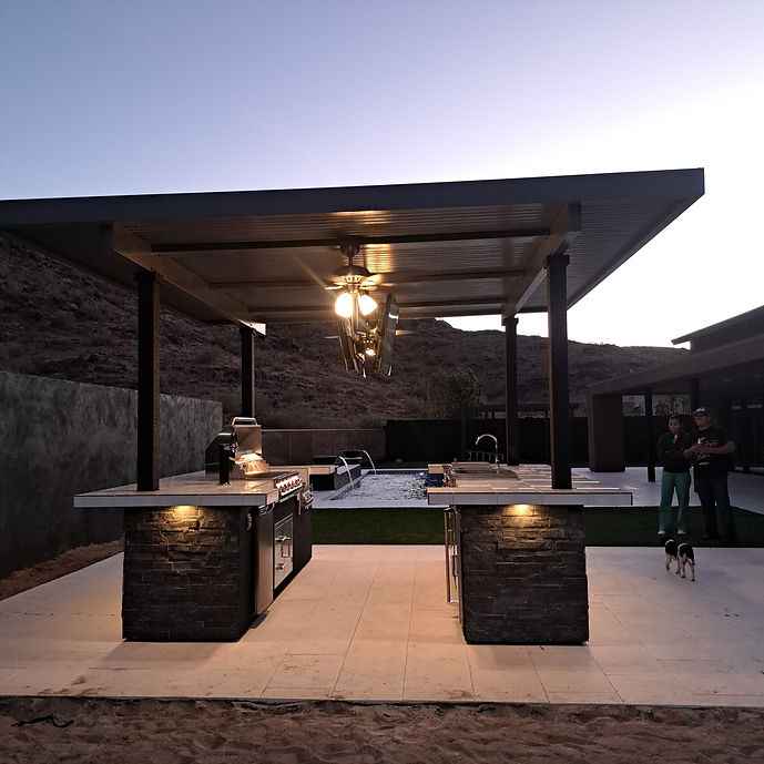 Wide view of the outdoor kitchen island with a mounted TV and built-in grill at dusk.