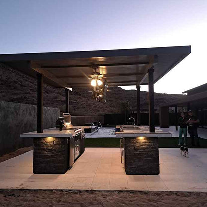 Wide view of the outdoor kitchen island with a mounted TV and built-in grill at dusk.