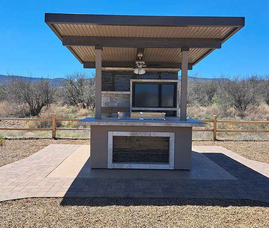 Covered outdoor kitchen island with a built-in gas grill on a paved patio.
