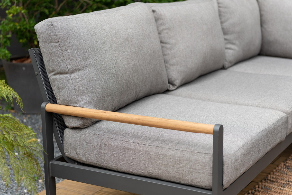 Close view of an outdoor sectional sofa with gray cushions, a dark frame, and a wood-tone armrest.
