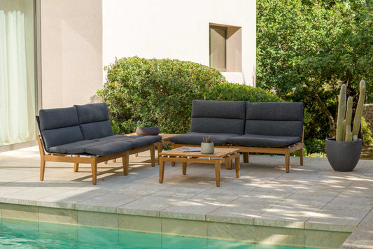 Dark-cushion outdoor seating arrangement with teak frames and side table on a patio.