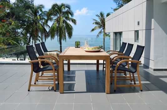  Teak dining table with black armchairs on a sunlit terrace overlooking the water.