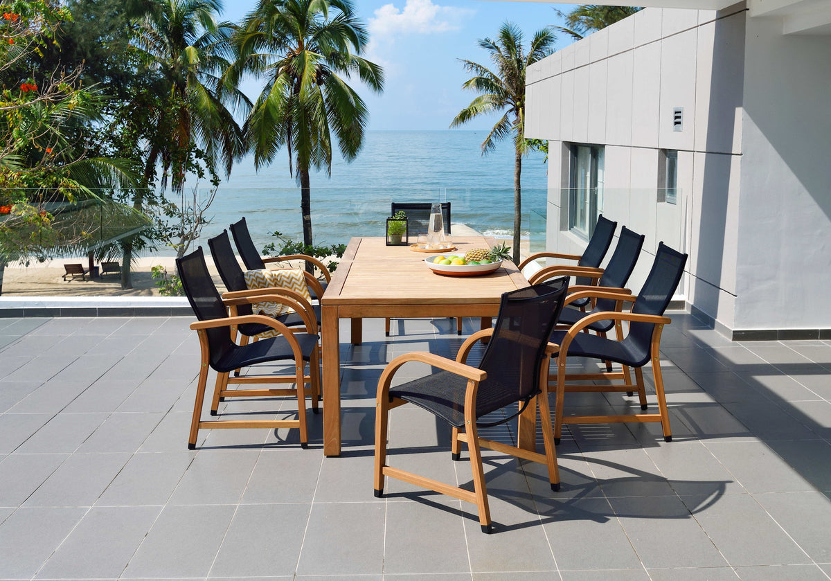 Outdoor dining set with an FSC teak table and eight black mesh armchairs beside a tropical ocean view.