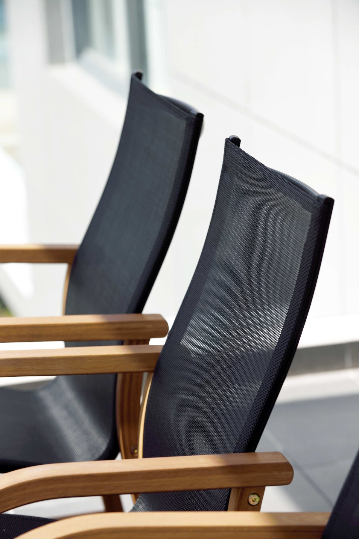 Close view of black Weather-net chair backs with wood armrests.

