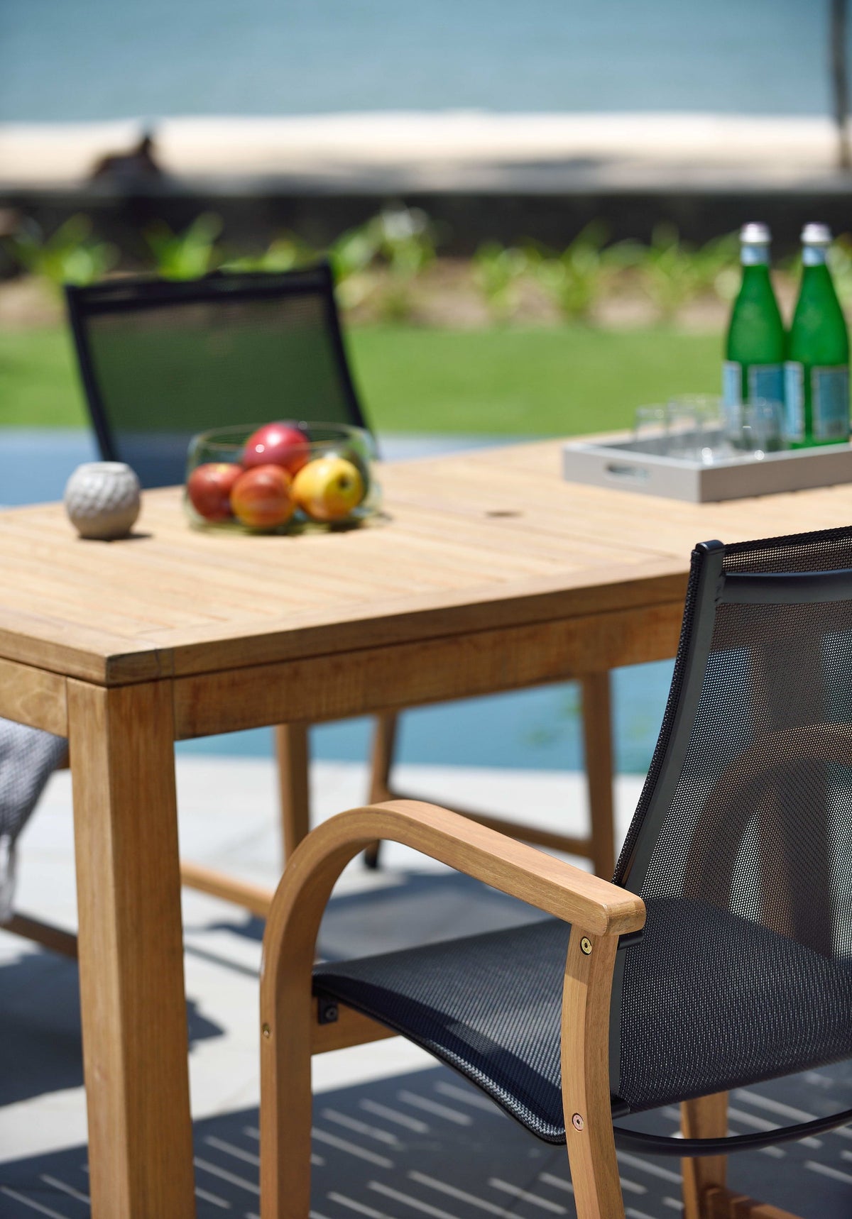 Close-up of an FSC teak tabletop and black armchair with a curved armrest.
