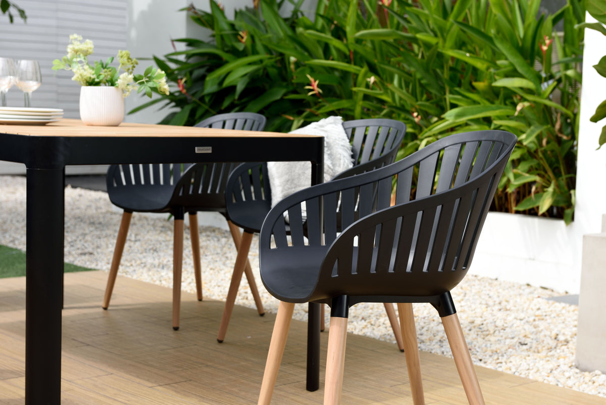 Rectangular teak dining table surrounded by black chairs in an outdoor setting.