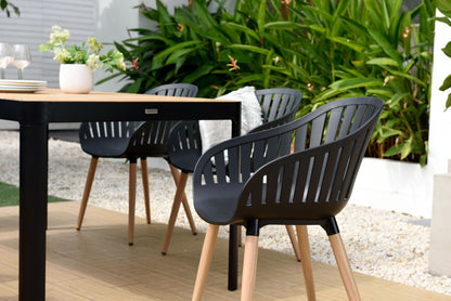 Rectangular teak dining table surrounded by black chairs in an outdoor setting.