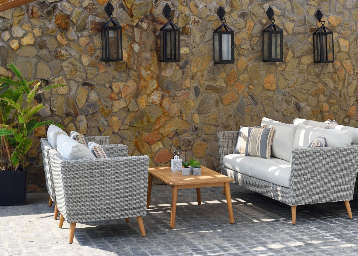 FSC eucalyptus wicker outdoor seating with cushions and a coffee table beside a stone wall.