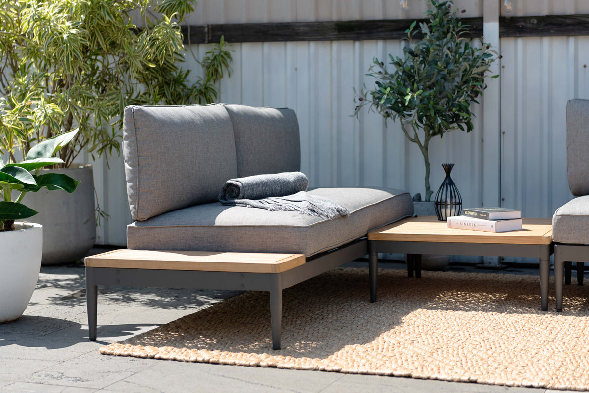Gray cushioned outdoor seating with a throw blanket, dark frames, a square coffee table, and wood-tone side surfaces.