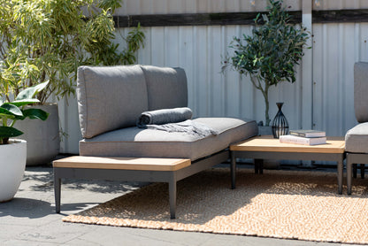 Gray cushioned outdoor seating with a throw blanket, dark frames, a square coffee table, and wood-tone side surfaces.