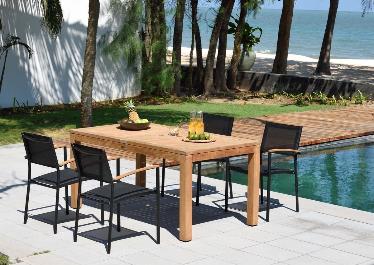 Teak outdoor dining table with four black stacking armchairs in an outdoor setting.