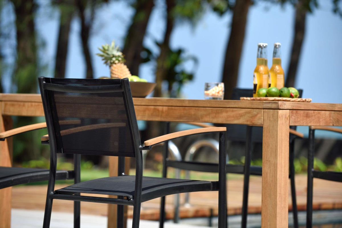 Close view of the teak table and black stacking armchairs.
