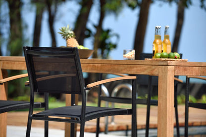 Close view of the teak table and black stacking armchairs.