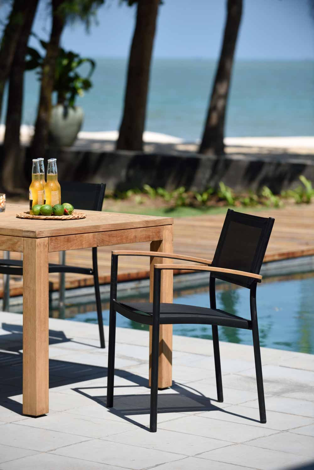 Outdoor dining set with a teak table and four black stacking armchairs.