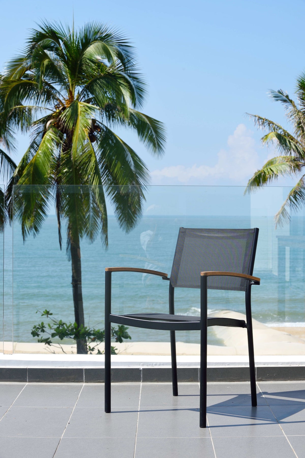 Detail of the black stacking armchair’s Weather-net seat and teak armrest.