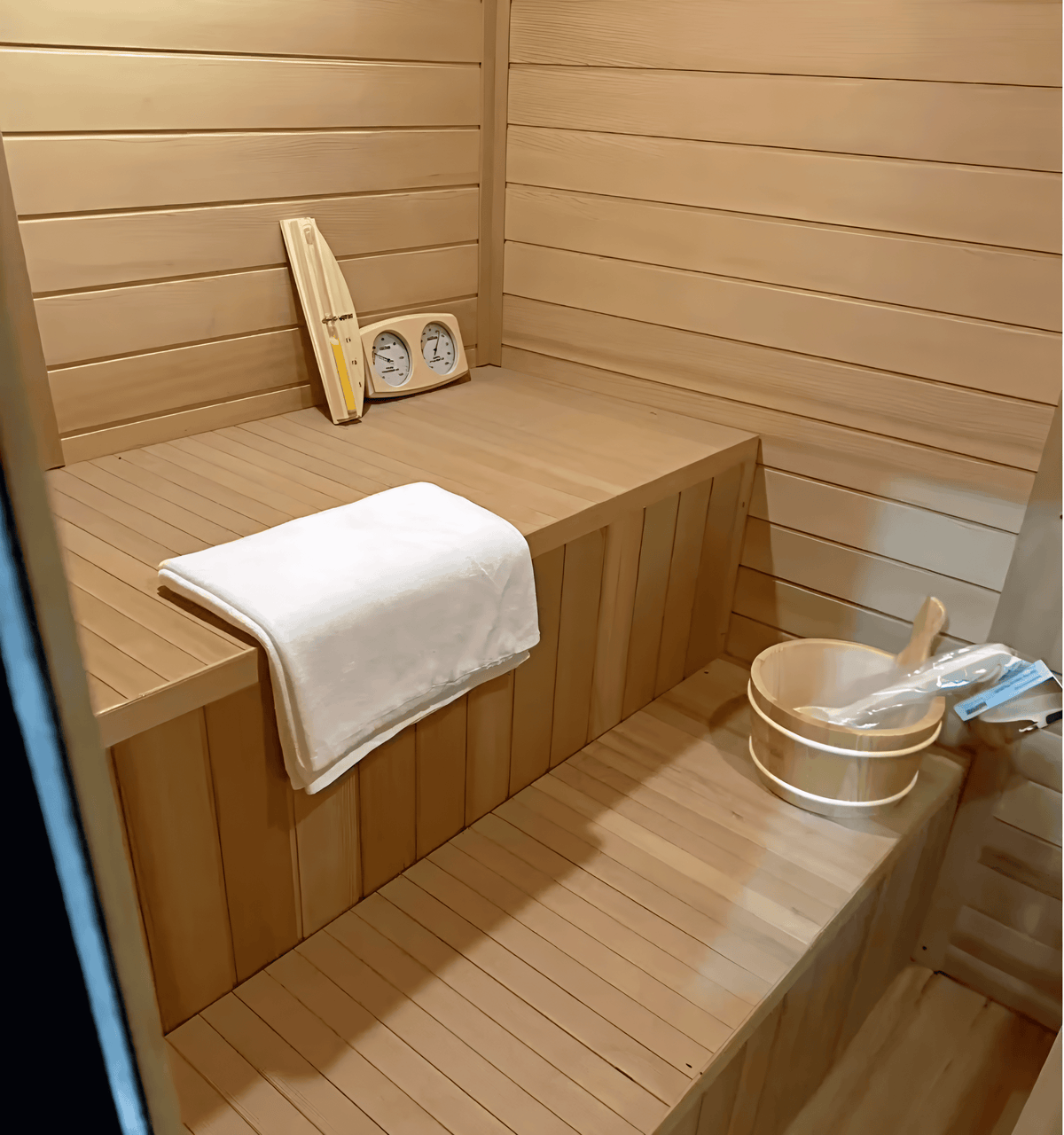Interior bench seating with towel, wooden bucket, and sauna gauges inside a hemlock sauna.